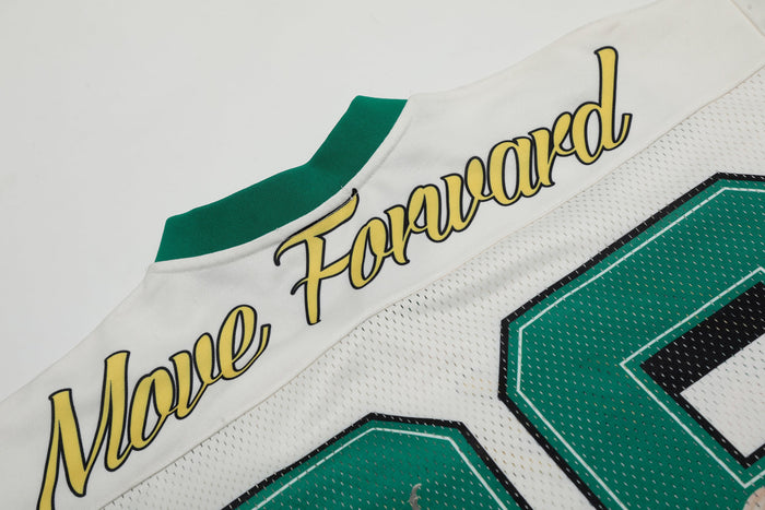 Close-up of a white football jersey with green accents and yellow script angel graphic in varsity streetwear style