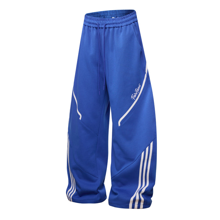 Royal blue track pants with white curved seam piping, side script logo, and striped lower leg