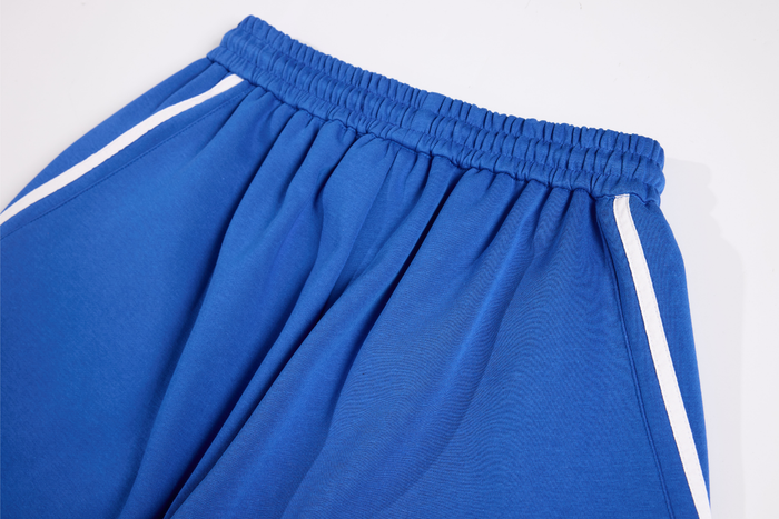 Close-up of royal blue track pants waistband with gathered elastic and white side stripe detail