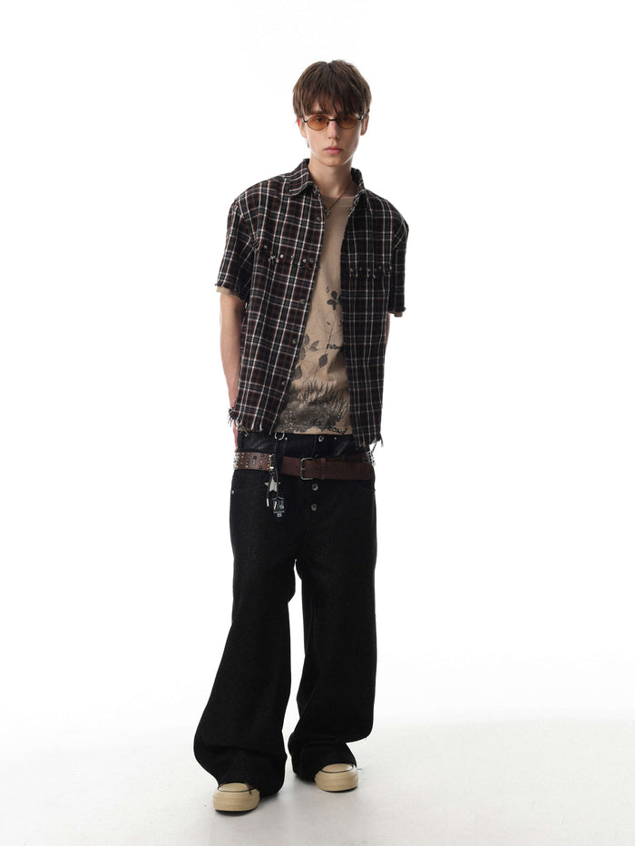 Model wearing a distressed black plaid short sleeve shirt with raw hem and streetwear styling on a white background