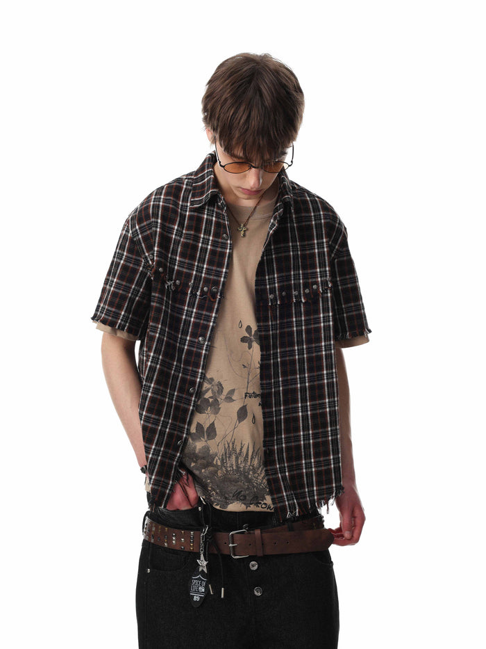 Distressed black plaid short sleeve shirt with raw frayed hems, worn over a graphic tee in a streetwear look