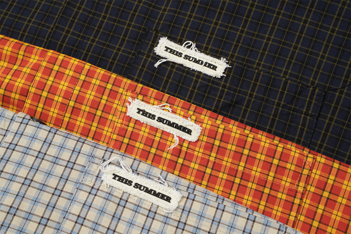 Close-up of embroidered THIS SUMMER labels on black, orange, and light blue plaid fabric