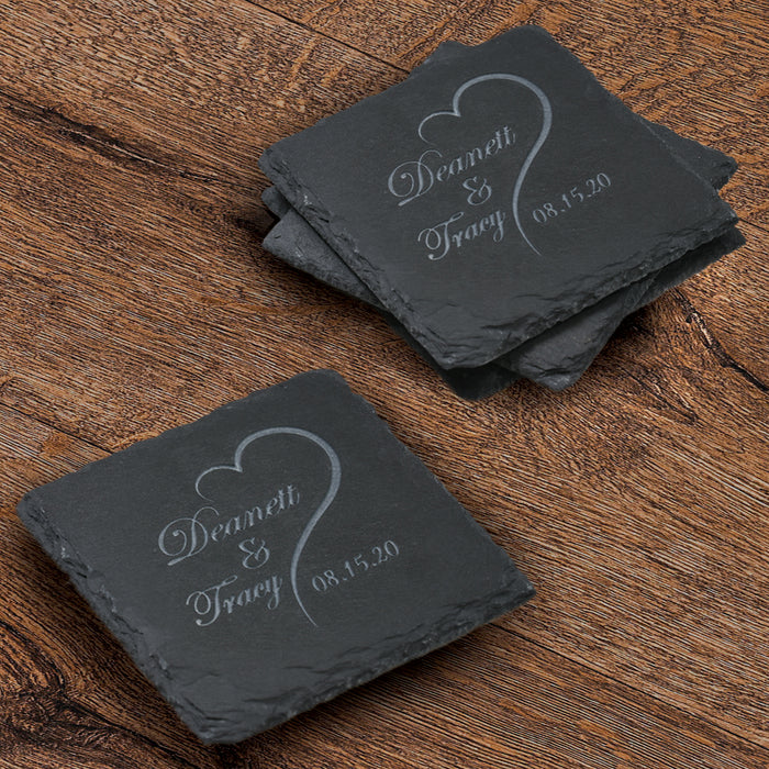 Stack of four square slate coasters deep-carved with two first names and a wedding date inside an open-heart outline.