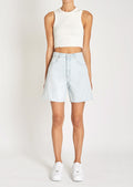 A woman in a white tank top, light-wash denim shorts, and sneakers.