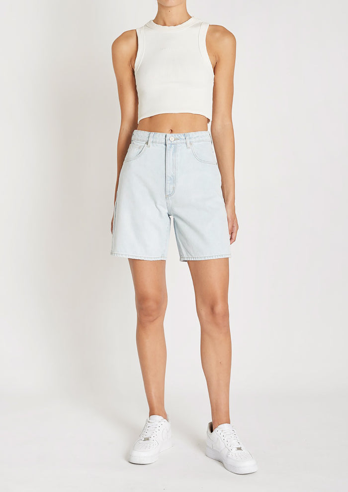 A woman in a white tank top, light-wash denim shorts, and sneakers.