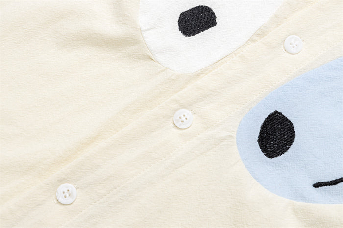 Close-up of white buttons along the cream shirt placket with partial dog graphic panels