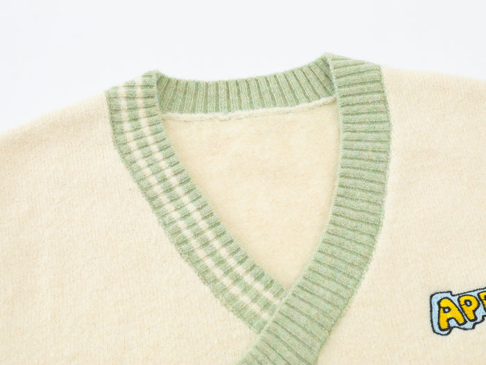 Close-up of the sage green ribbed V-neck trim on the cream knit sweater vest