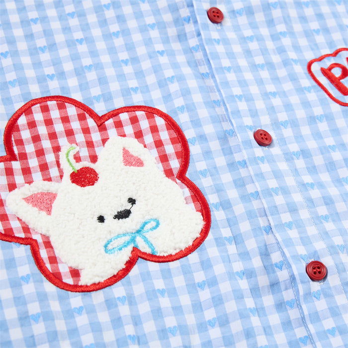 Close-up of a textured cartoon animal patch on blue gingham fabric with red buttons and heart-patterned checks