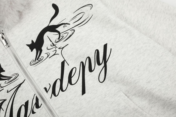 Close-up of a black cat graphic and script lettering beside the silver front zipper on the light gray hoodie