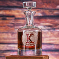 A glass spirits decanter with a faceted stopper, filled with amber spirit, deep-carved with a single block initial in a circle.