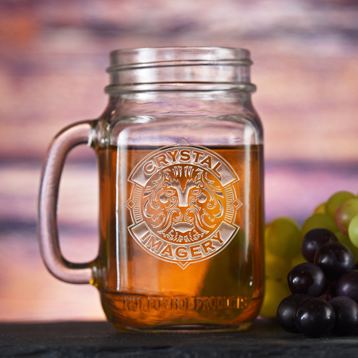 Mason jar mug with a handle, filled with an amber drink, sand-carved with a sample Crystal Imagery crest where your logo would go.