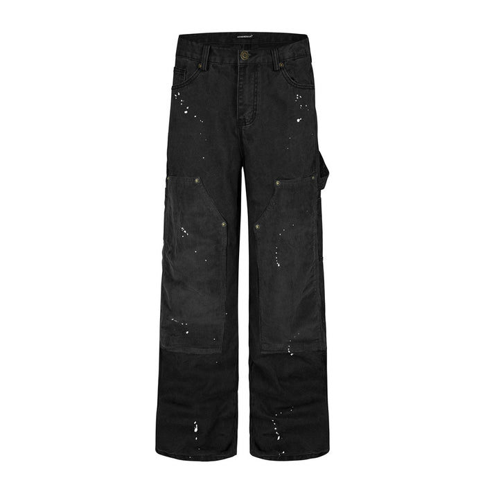 Front view of black wide-leg carpenter pants with large corduroy knee patches, utility pockets, and scattered white paint marks