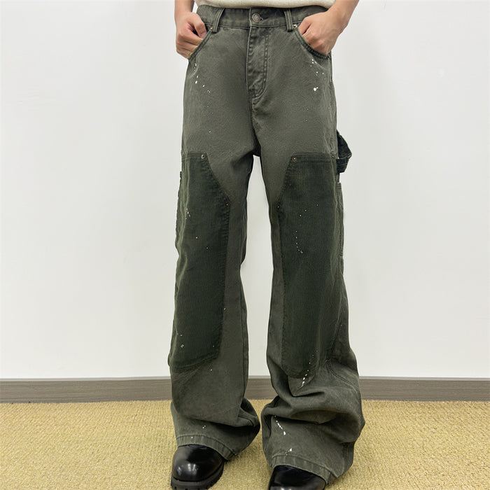 Front view of olive green carpenter pants worn on a model with dark corduroy knee patches and white paint splatters
