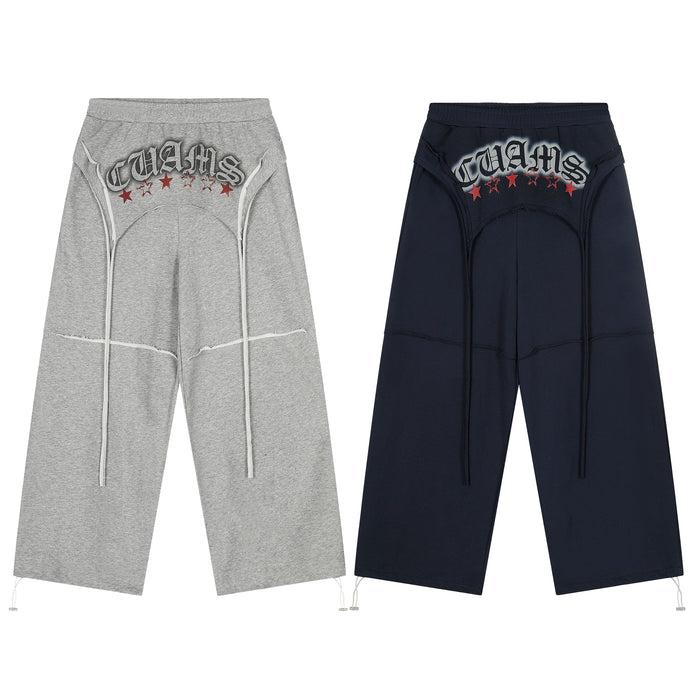 CUAMS grey and navy wide-leg sweatpants with embroidered lettering, red stars, and white multi-drawstring front detailing