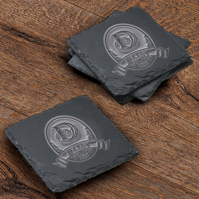 Stack of four square slate coasters deep-carved with an initial in an ornate rounded crest above a name banner.