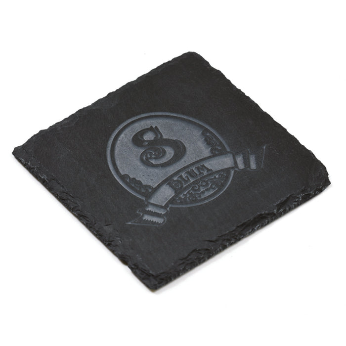 Close-up of one square slate coaster deep-carved with an initial in an ornate crest and a name banner.