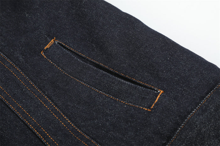 Close-up of a dark denim jacket welt pocket with contrasting orange stitching