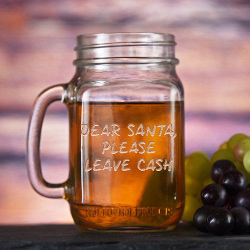 Mason jar mug with a handle, sand-carved with the words "Dear Santa, Please Leave Cash" in hand-lettered capitals.