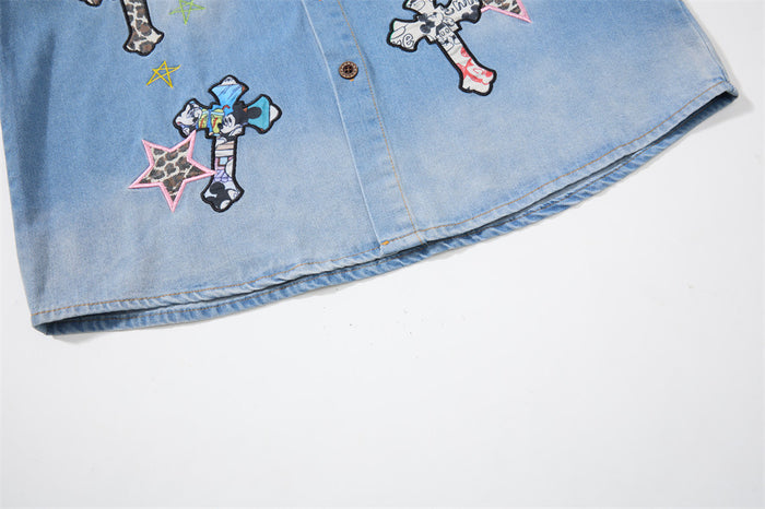 Lower front of the light blue denim shirt with colorful embroidered patches and stitched hem