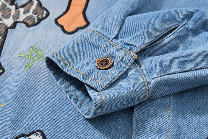 Close-up of a denim shirt cuff with a brown button, contrast stitching, and embroidered graphics