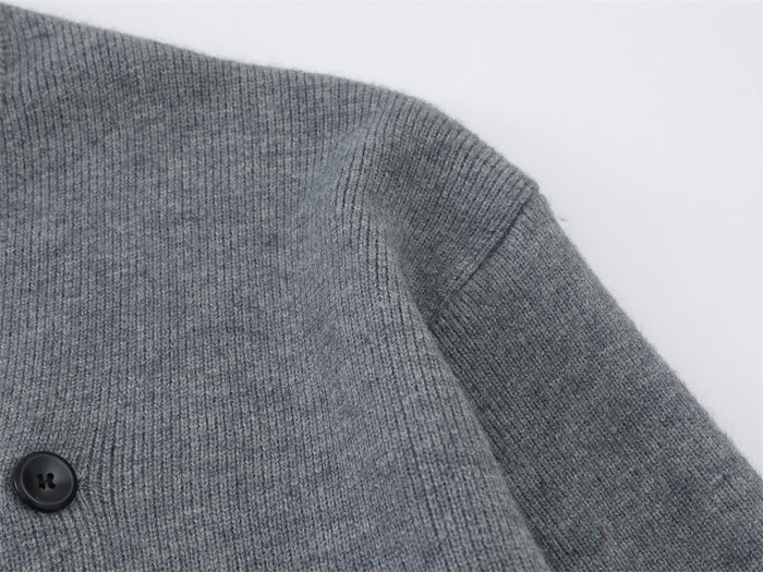 Close-up of gray knit cardigan shoulder and sleeve seam with a dark button visible on the front panel