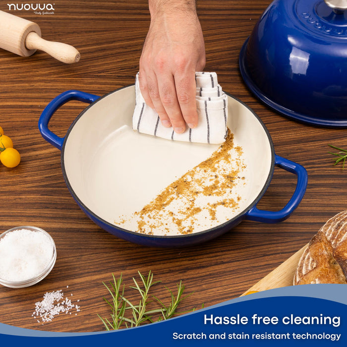 Person cleaning a blue enameled cast iron bread towel with a dish towel as it promises hassle free cleaning with scratch and stain resistant technology.
