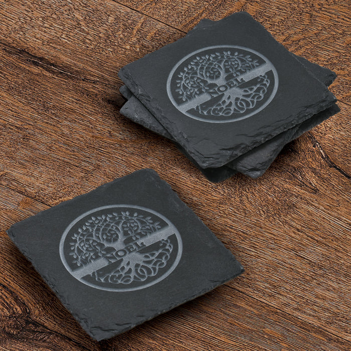 Stack of four square slate coasters deep-carved with a Celtic tree-of-life design and a family name in a circular knotwork ring.