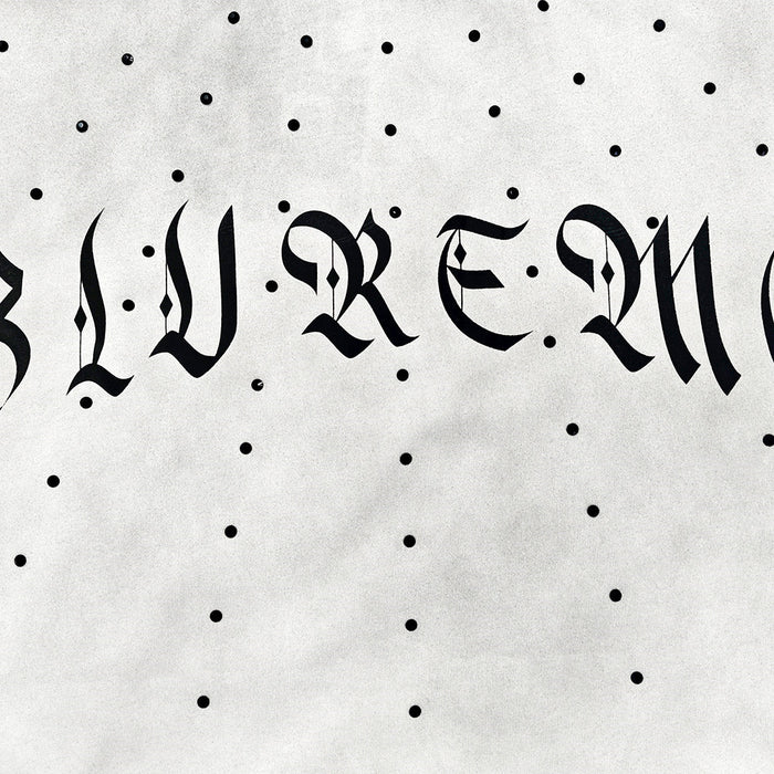 White oversized washed T-shirt with black gothic lettering and scattered polka-dot print, featuring a distressed streetwear look