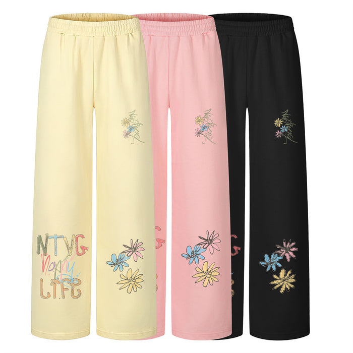 Three pairs of wide-leg sweatpants in pale yellow, pink, and black with floral graffiti prints and elastic waists