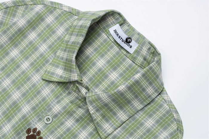 Close-up of the green plaid shirt collar, woven label, top button, and paw-print embroidery