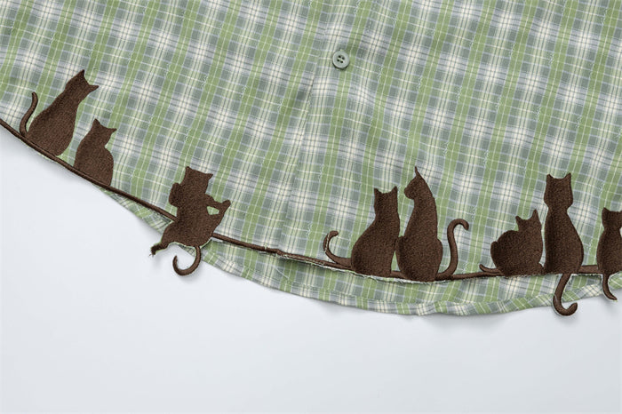 Close-up of the green plaid shirt hem with a row of brown embroidered cats and tails