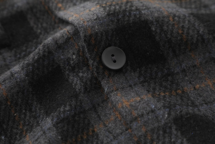 Close-up of black button on dark plaid flannel fabric with soft brushed texture