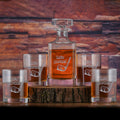 A square whiskey decanter and four rocks glasses, each deep-carved with "Let's par-tee!" and a golf club and ball, filled with amber spirit on a wood slab.