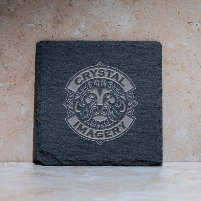 Square slate coaster deep-carved with a sample Crystal Imagery crest where your custom logo or monogram would be carved, standing against stone.