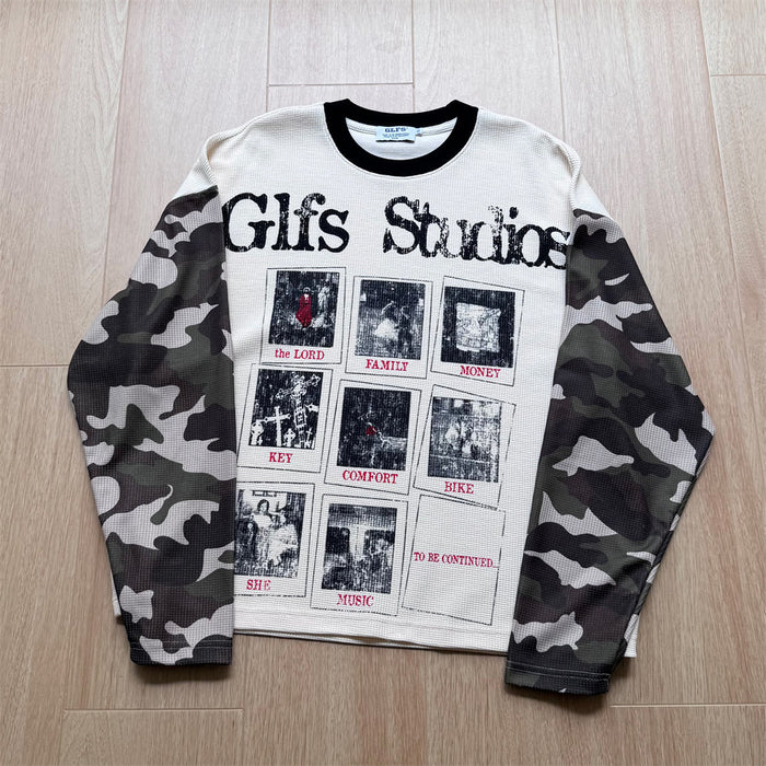 Flat-lay front view of a cream graphic shirt with camo sleeves and illustrated text-and-panel design
