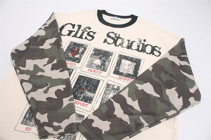 Folded shirt detail showing overlapping camouflage sleeves, cream waffle-knit body, and front graphic