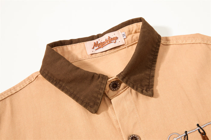 Close-up of the tan shirt front showing its dark brown textured collar, button placket, and chest embroidery
