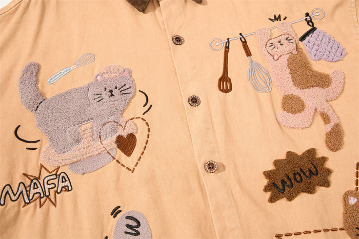 Tan shirt front with embroidered cartoon cats, kitchen utensils, speech bubbles, and decorative lettering