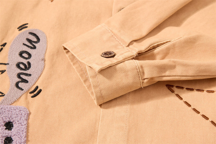 Close-up of the tan shirt sleeve cuff showing its button fastening and fine woven texture