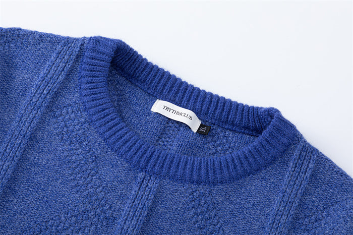 Close-up of the blue sweater's ribbed crew neckline, inner label, and diamond cable knit texture