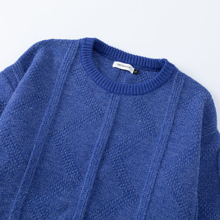 Upper front detail of a blue crewneck sweater showing the ribbed collar and raised diamond knit panels