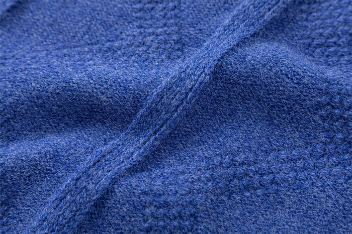 Close-up of blue knitted sweater fabric showing raised cable lines and soft textured diamond pattern