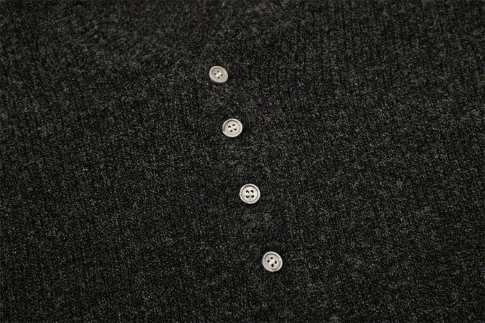 Close-up of four light-colored buttons on the dark charcoal knit Henley placket