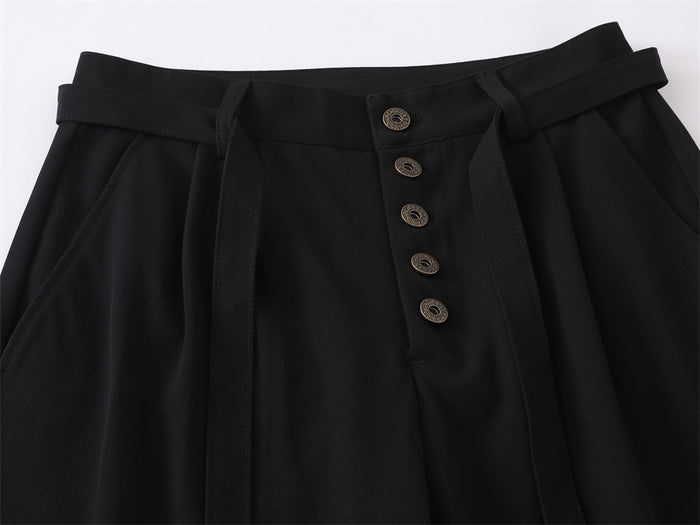 Close-up of black trouser waistband with pleats, belt tabs, adjustable belt, and five-button fly