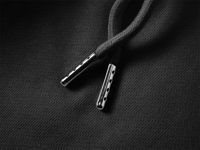 Close-up of black drawstring ends with silver metal aglets against textured fabric