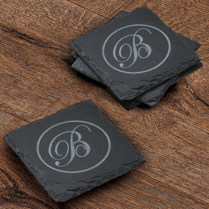 Stack of four square slate coasters deep-carved with a single script initial inside a thin circle.