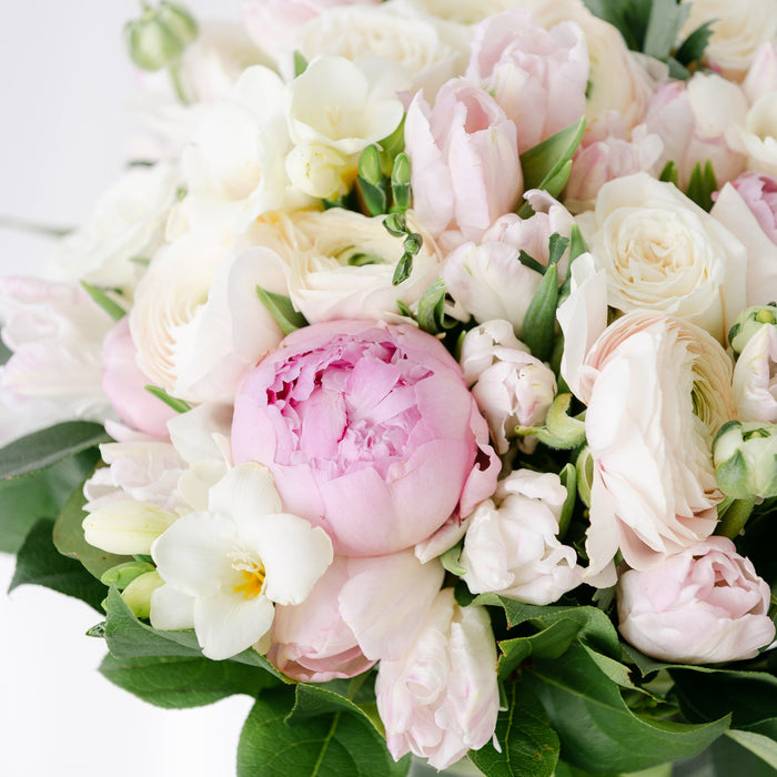 a white and pink floral arrangement of parrot tulips, persian tulips, ranunculus, and peonies.