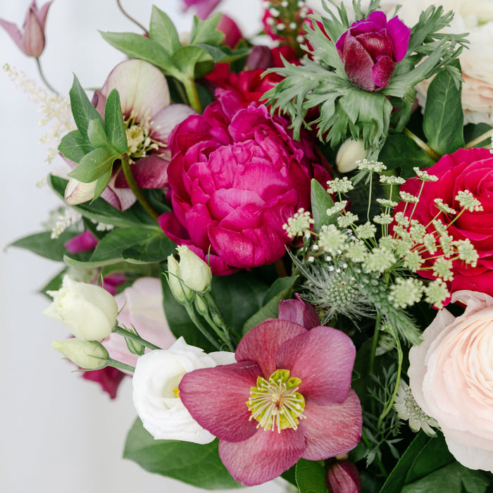 an arrangement of flowers including peony, white roses, lenten rose, queen annes lace, thistle.