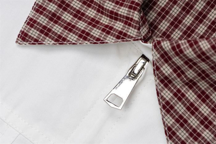 Detailed view of the burgundy plaid collar and shiny metal zipper on the white jacket