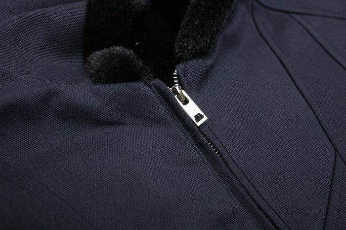 Close-up of the navy bomber jacket zipper beside the black plush-lined hood